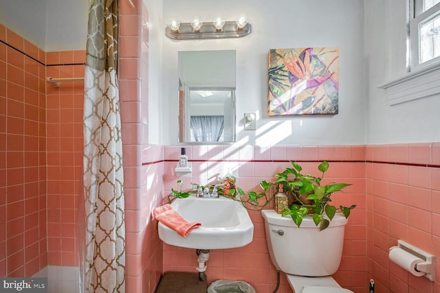 full bath with tile walls, wainscoting, toilet, curtained shower, and a sink