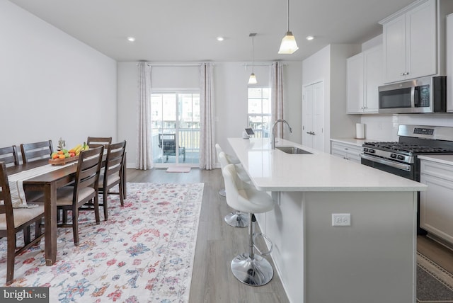 kitchen featuring pendant lighting, sink, stainless steel appliances, light hardwood / wood-style floors, and a center island with sink