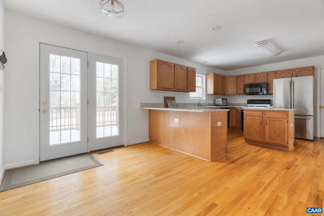 kitchen featuring stainless steel refrigerator, sink, stove, kitchen peninsula, and light wood-type flooring