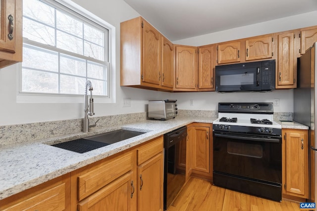 kitchen featuring light stone countertops, sink, light hardwood / wood-style floors, and black appliances