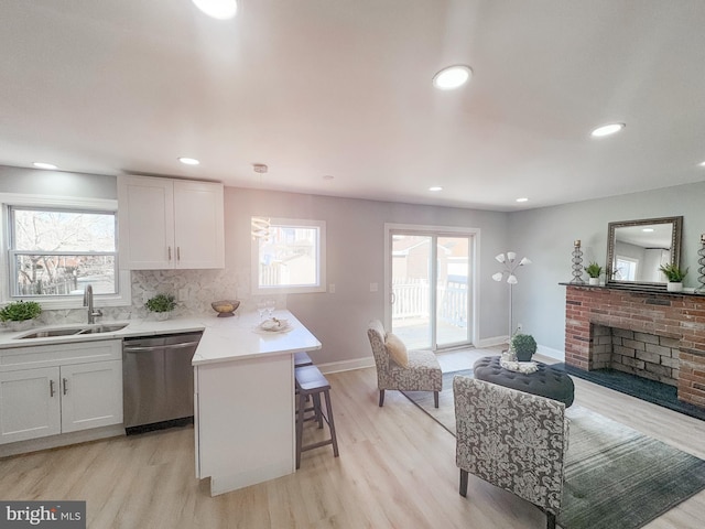 kitchen featuring sink, a brick fireplace, dishwasher, white cabinets, and backsplash