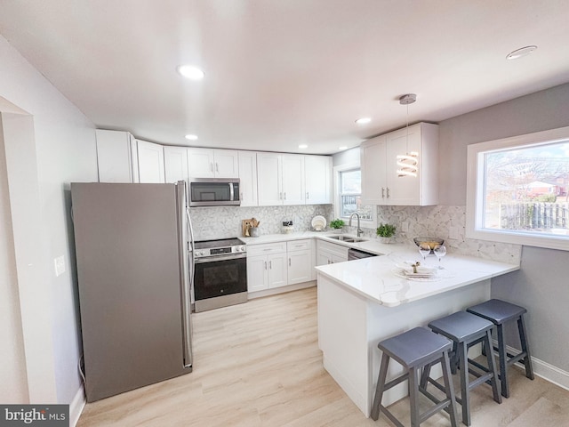 kitchen featuring sink, hanging light fixtures, appliances with stainless steel finishes, kitchen peninsula, and white cabinets