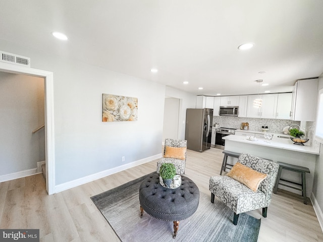 interior space featuring white cabinetry, tasteful backsplash, appliances with stainless steel finishes, pendant lighting, and light hardwood / wood-style floors