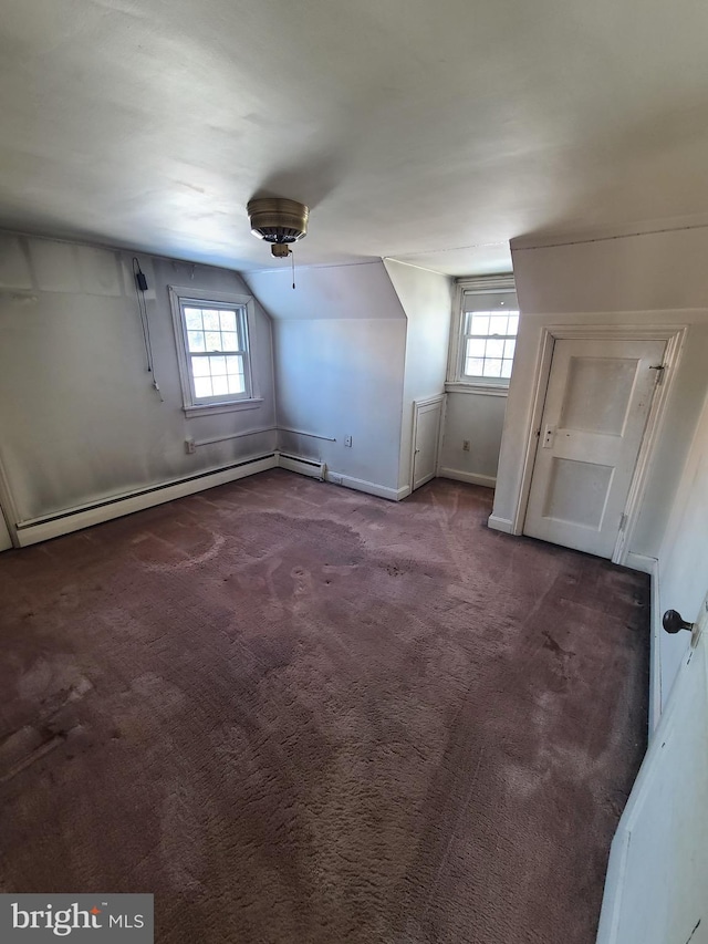 additional living space with baseboard heating, lofted ceiling, dark carpet, and a wealth of natural light