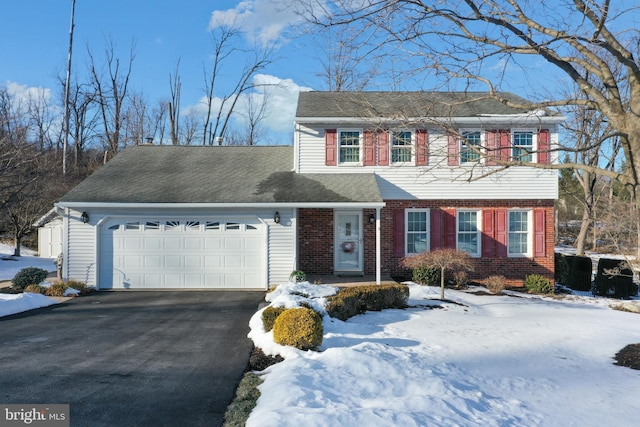 colonial-style house with aphalt driveway, an attached garage, brick siding, and a shingled roof