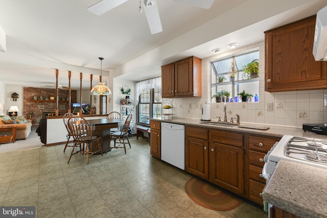 kitchen with a fireplace, white dishwasher, a sink, tasteful backsplash, and brown cabinets