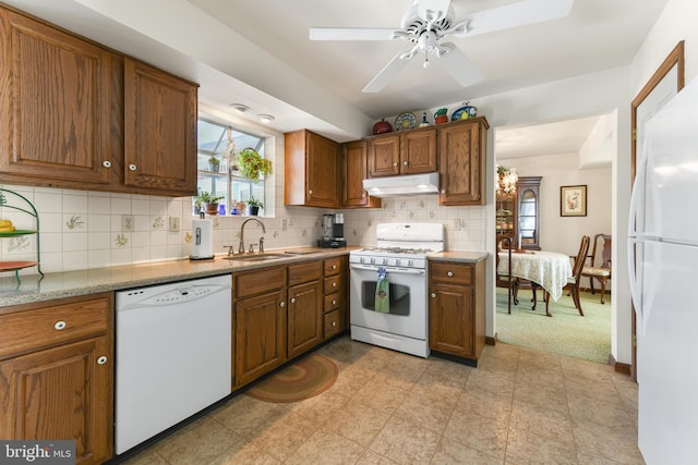 kitchen featuring under cabinet range hood, a sink, backsplash, white appliances, and brown cabinetry