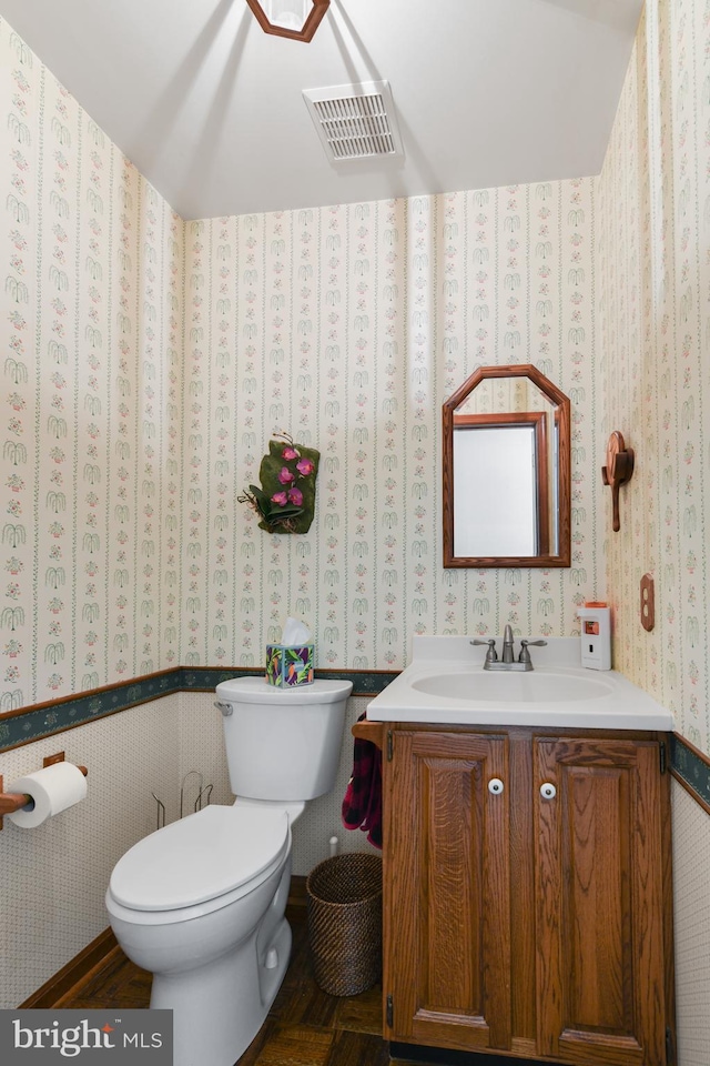 bathroom with wallpapered walls, toilet, vanity, and visible vents