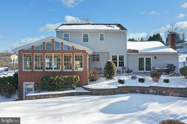 snow covered back of property with french doors and brick siding