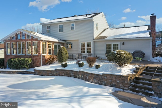 snow covered rear of property featuring a chimney