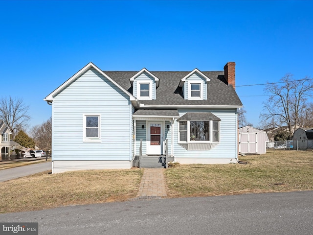 new england style home with roof with shingles, a chimney, a storage shed, a front yard, and an outdoor structure