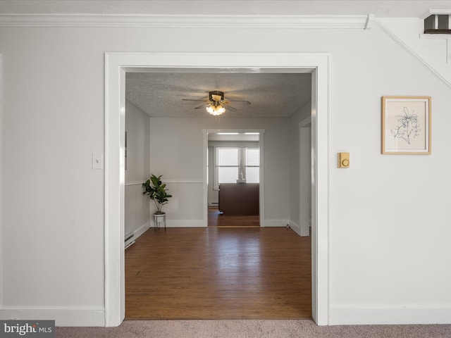 hall featuring a textured ceiling, crown molding, wood finished floors, and baseboards