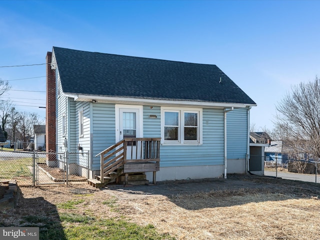 view of front facade featuring a shingled roof, fence, and a gate