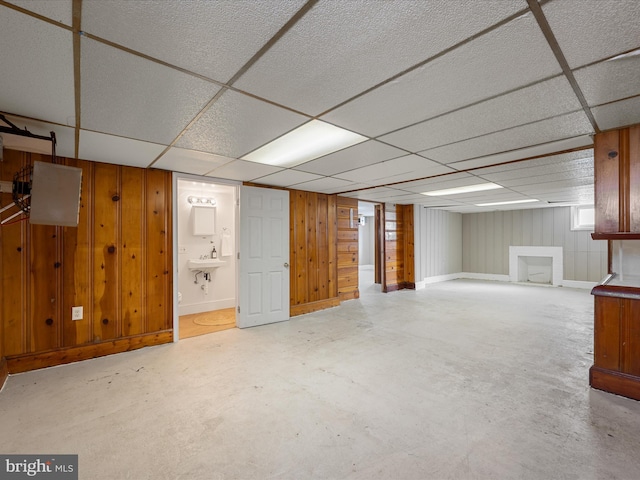 finished basement with a paneled ceiling, wood walls, baseboards, and a sink