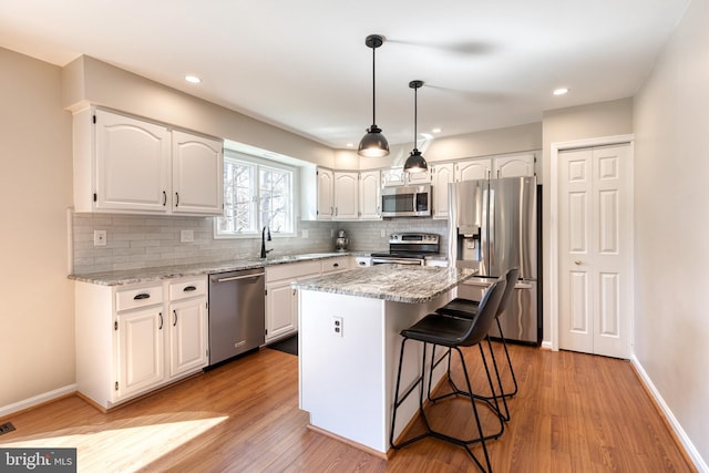 kitchen featuring light stone counters, stainless steel appliances, a sink, white cabinets, and light wood finished floors