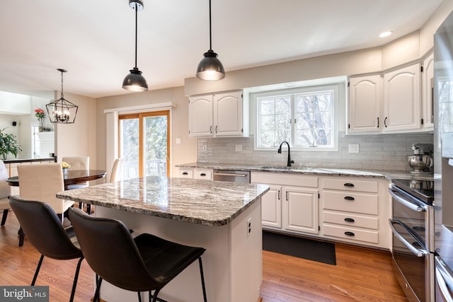 kitchen with stainless steel appliances, a kitchen island, white cabinetry, light wood-style floors, and light stone countertops