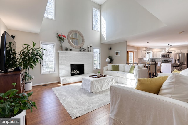 living room with baseboards, visible vents, wood finished floors, a high ceiling, and a fireplace