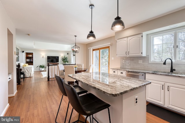 kitchen featuring light wood finished floors, white cabinets, decorative backsplash, a sink, and stainless steel dishwasher