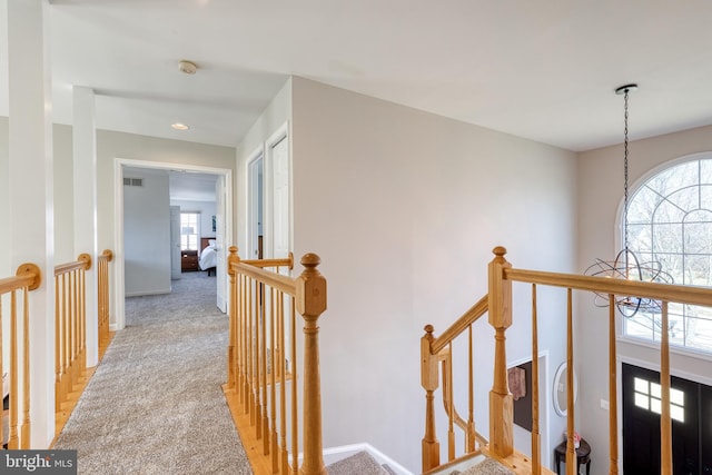 hallway with baseboards, light colored carpet, visible vents, and an upstairs landing