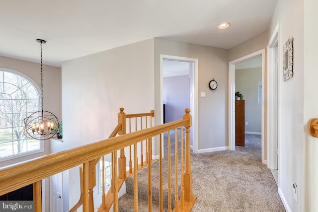 corridor featuring carpet floors, an inviting chandelier, baseboards, and an upstairs landing