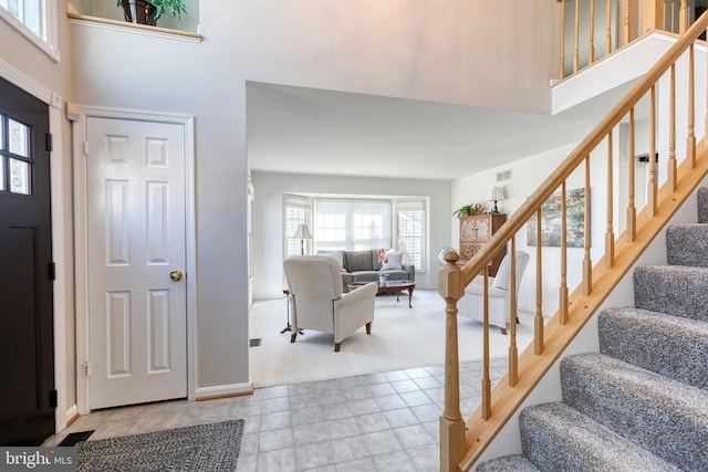 foyer featuring light tile patterned floors, light carpet, a high ceiling, visible vents, and stairs