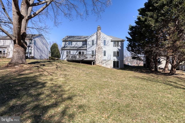 back of house featuring a chimney, a wooden deck, and a lawn