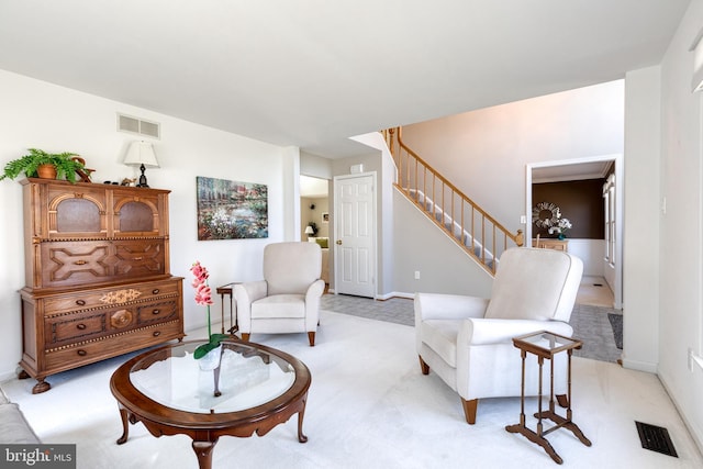 living area featuring light carpet, stairway, and visible vents