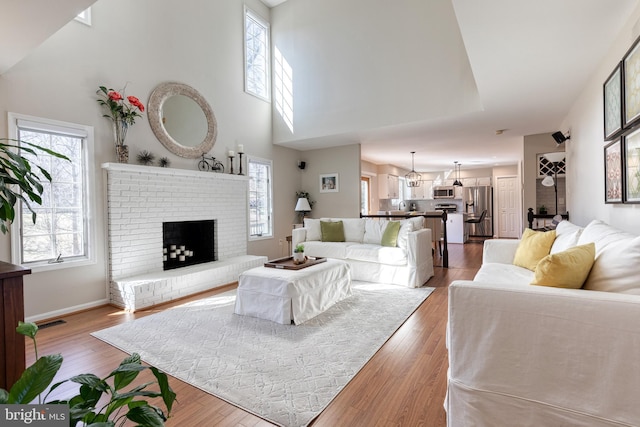 living area featuring a fireplace, a towering ceiling, baseboards, and wood finished floors