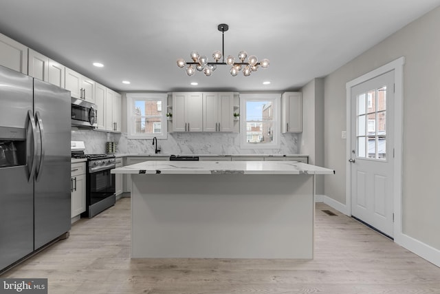 kitchen with white cabinetry, hanging light fixtures, stainless steel appliances, a center island, and light stone countertops