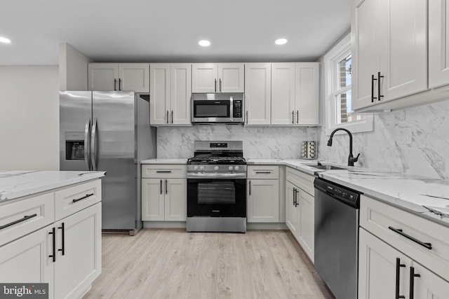 kitchen featuring sink, white cabinetry, stainless steel appliances, light stone countertops, and light wood-type flooring