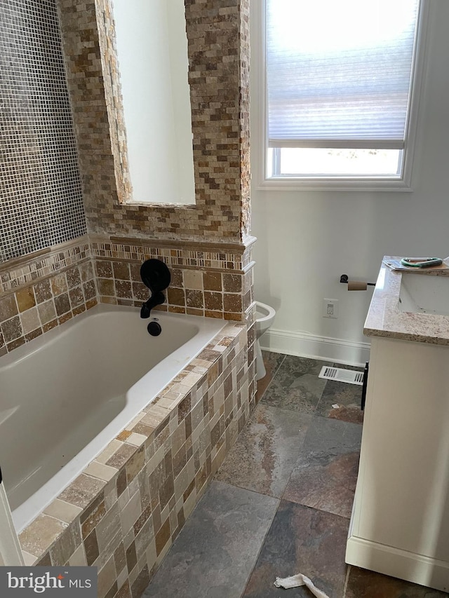 bathroom featuring vanity, a relaxing tiled tub, and toilet