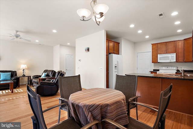 dining area with ceiling fan with notable chandelier, sink, and light hardwood / wood-style flooring