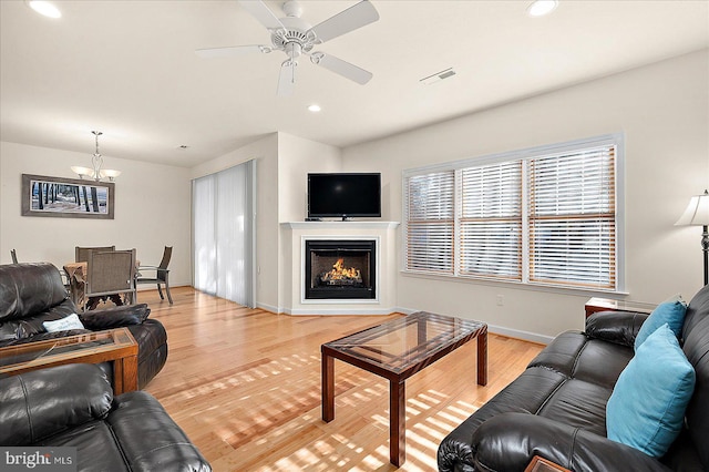 living room with ceiling fan with notable chandelier and light hardwood / wood-style flooring