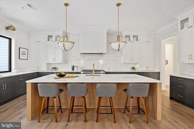 kitchen with hanging light fixtures, backsplash, white cabinets, and a center island with sink