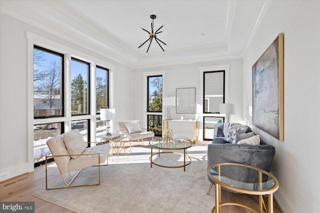 living area with a raised ceiling, wood finished floors, visible vents, and baseboards