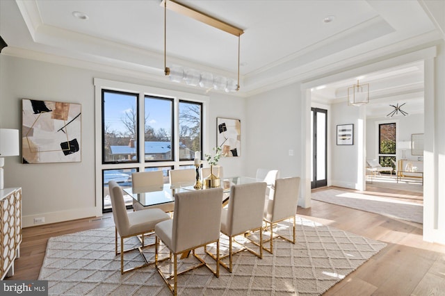 dining room with ornamental molding, a tray ceiling, baseboards, and light wood finished floors