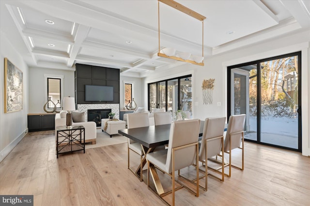 dining area with beamed ceiling, coffered ceiling, a fireplace, and light hardwood / wood-style flooring