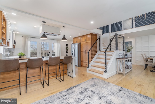 kitchen with stainless steel refrigerator with ice dispenser, a breakfast bar area, hanging light fixtures, light hardwood / wood-style floors, and backsplash