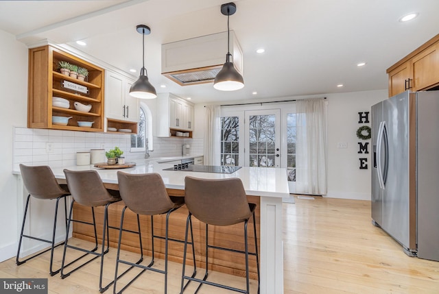 kitchen with kitchen peninsula, white cabinets, a kitchen bar, black electric stovetop, and stainless steel fridge with ice dispenser