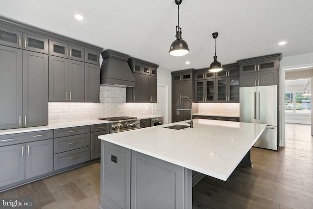 kitchen featuring pendant lighting, sink, premium appliances, a kitchen island with sink, and custom range hood