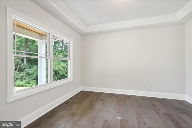 empty room with a tray ceiling, dark wood-type flooring, and ornamental molding