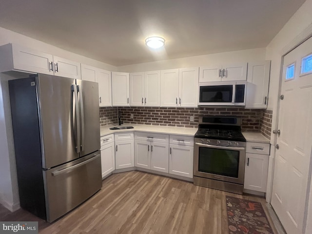 kitchen with sink, appliances with stainless steel finishes, backsplash, white cabinets, and light wood-type flooring