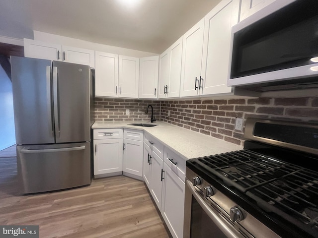 kitchen featuring sink, white cabinetry, light wood-type flooring, appliances with stainless steel finishes, and backsplash