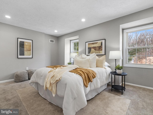 bedroom with multiple windows, light colored carpet, and a textured ceiling