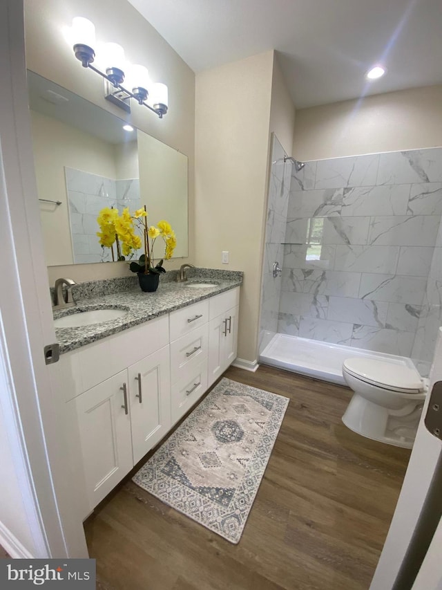 full bath with tiled shower, a sink, toilet, and wood finished floors