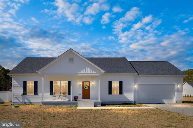 view of front of house featuring a porch, roof with shingles, an attached garage, gravel driveway, and a front lawn