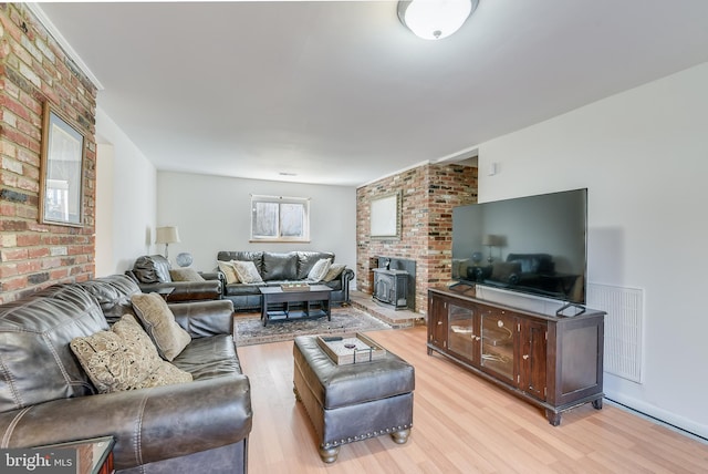 living area featuring a wood stove, brick wall, light wood-style flooring, and visible vents