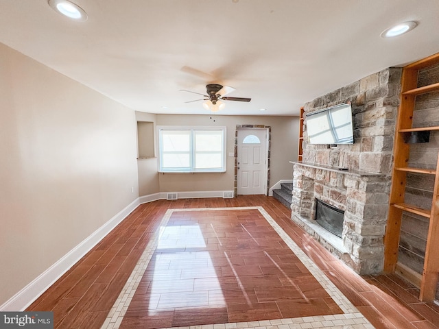 unfurnished living room featuring hardwood / wood-style flooring, a stone fireplace, and ceiling fan