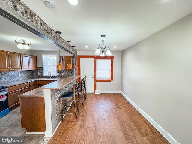 kitchen featuring sink, a kitchen bar, dark stone counters, hanging light fixtures, and decorative backsplash