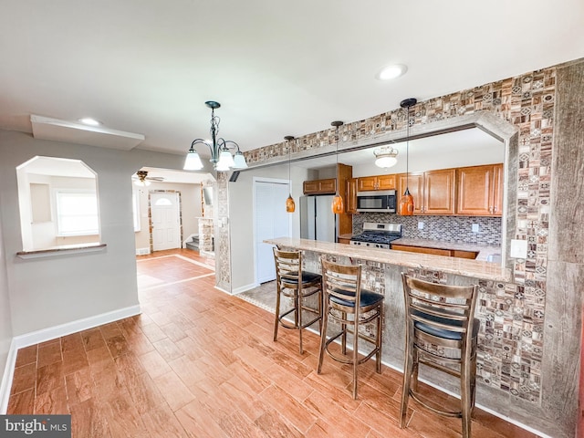 kitchen featuring a kitchen bar, light stone counters, light wood-type flooring, appliances with stainless steel finishes, and backsplash